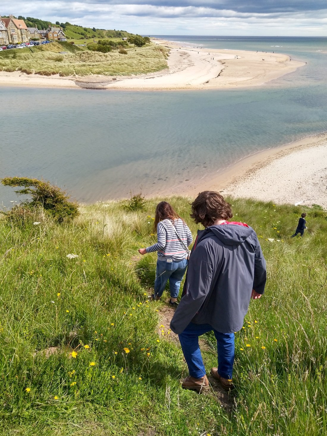 Three people walking down a steep path to a beach