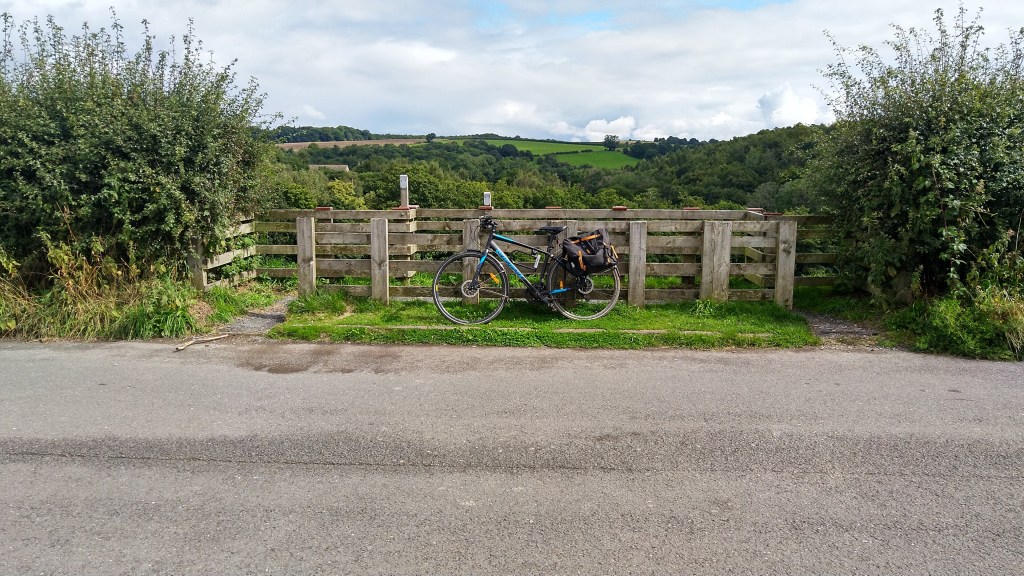 Bike leaning on fence by side of road with fields and hills in the distance