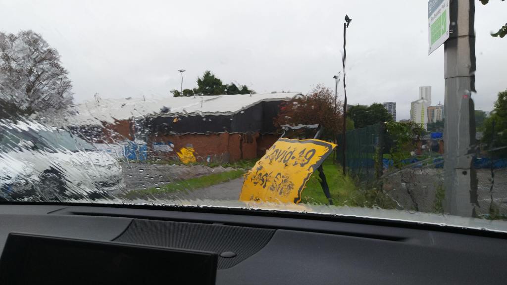 Scene through rainy car window includes a sign for a COVID-19 Test Centre