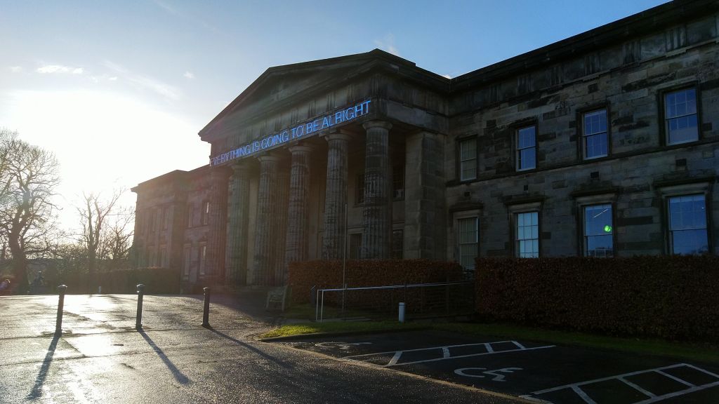 Classical building with portico. Across the top of the portico are the words in neon letters: Everything is going to be alright"