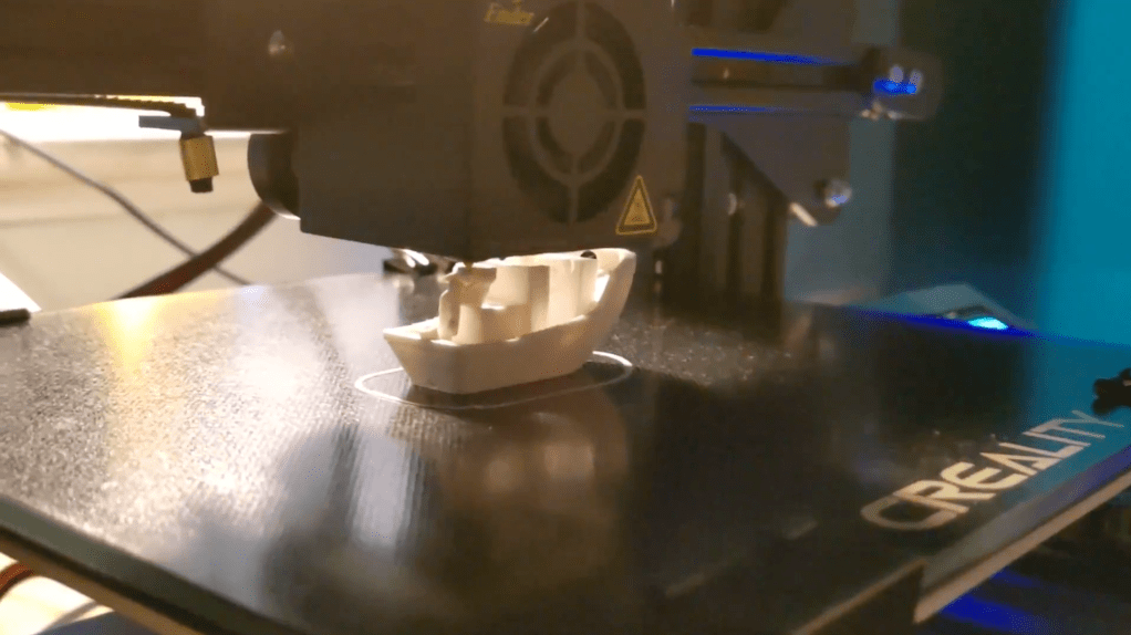 3d printer printing a tiny white plastic boat