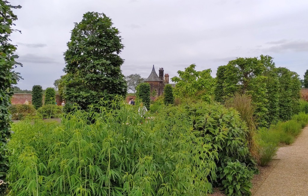 Trees and gardens in front of a stone building with cylindrical tower