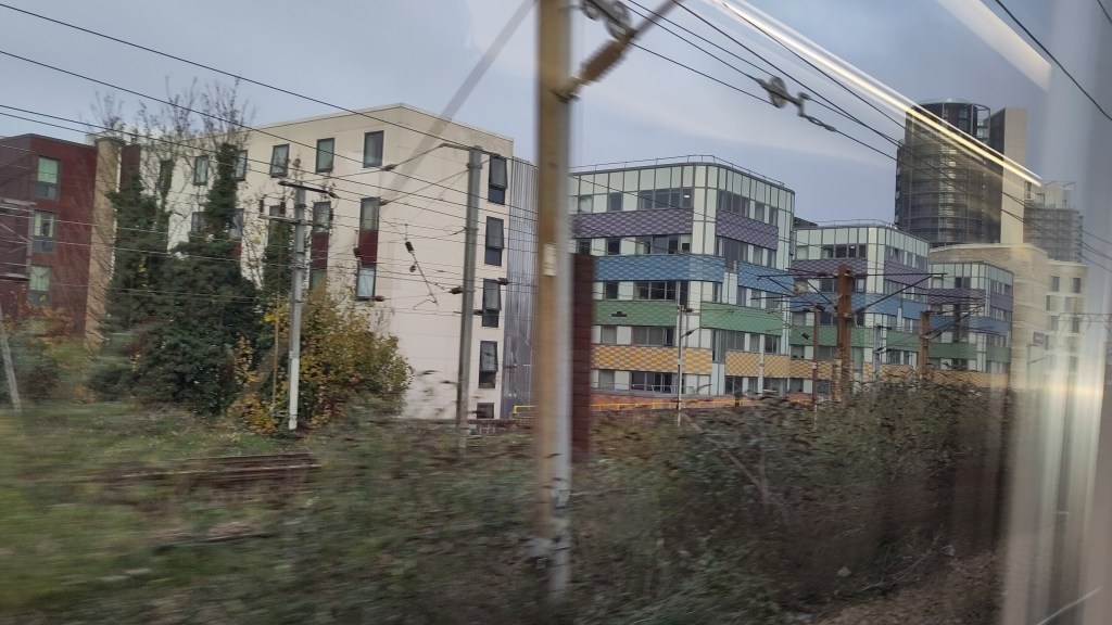 View from train, modern blocks of flats seen beyond electric wires and gantrys