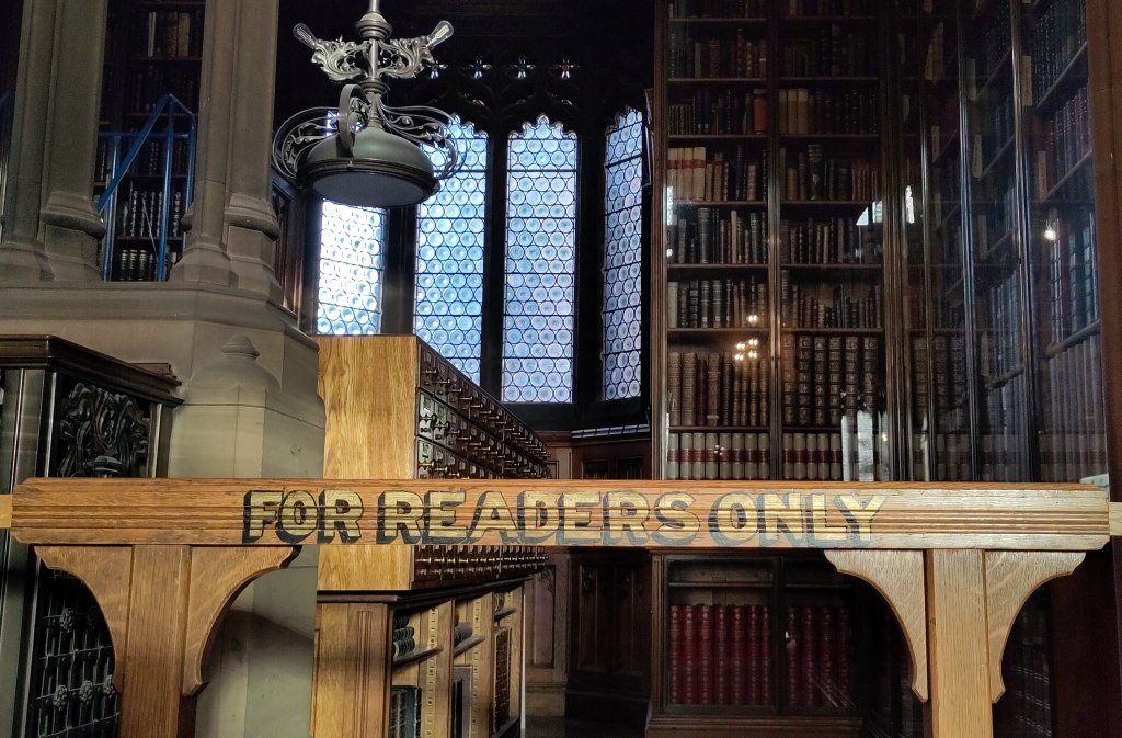 View of a Gothic Library interior with wooden card index cases. in the foreground a wooden bar with hand-lettered words 'FOR READERS ONLY' highlighted in gold