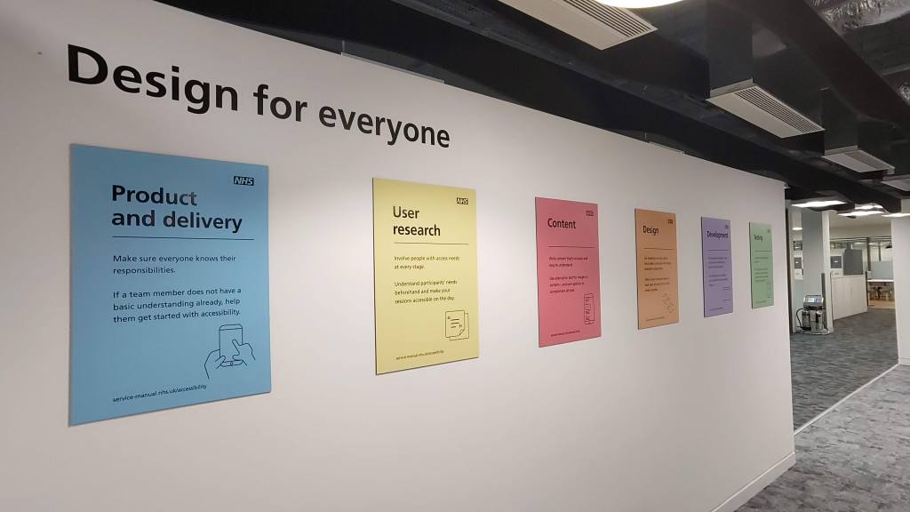 An internal office wall with the words "Design for everyone" and coloured posters in a row underneath 