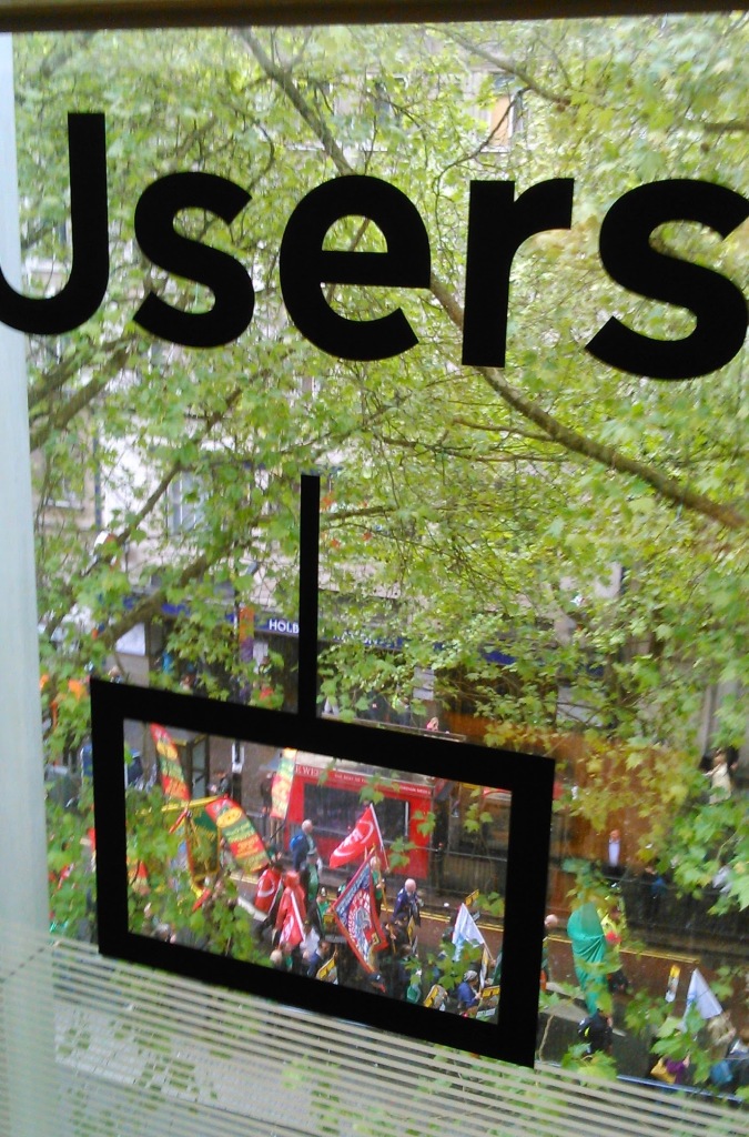 A view from a window with the word "Users" on the window in big black writing. Below the word, a black line leads to a rectangular box on the window, and through the box can be seen a group of people holding flags and banners