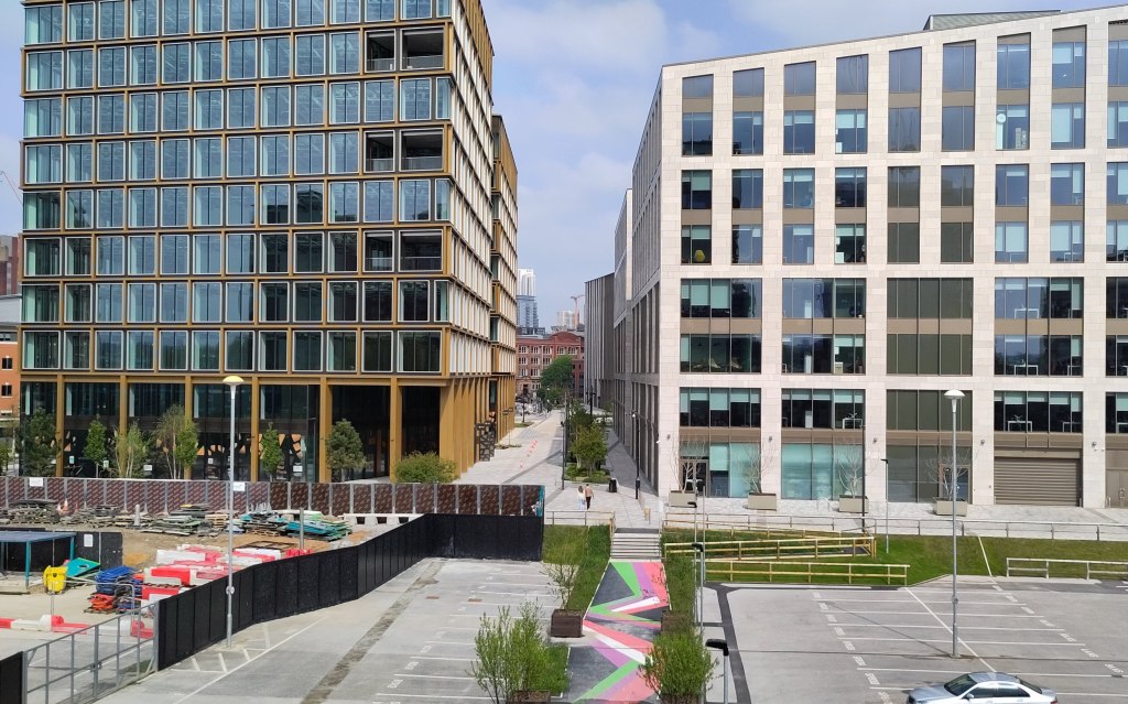 Two new build office blocks with a pedestrian boulevard bwtween them. In th foreground, a path flanked by small tree is painted in a colourful zig-zag pattern