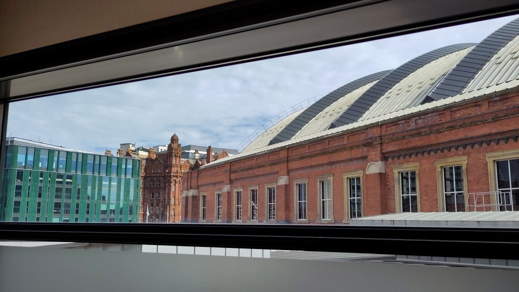 View through a narrow, horizontal window to a substantial brick-built former railway station with glass roof