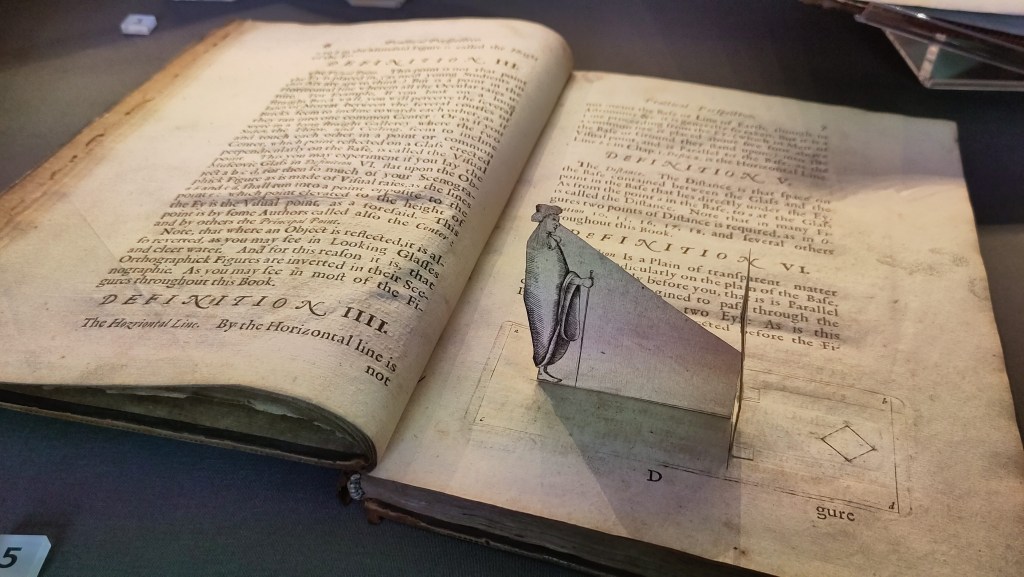 A 17th Century book open at a page with printed text and a pop-up human profile with a diagonal paper cutout descending from the person's eyeline