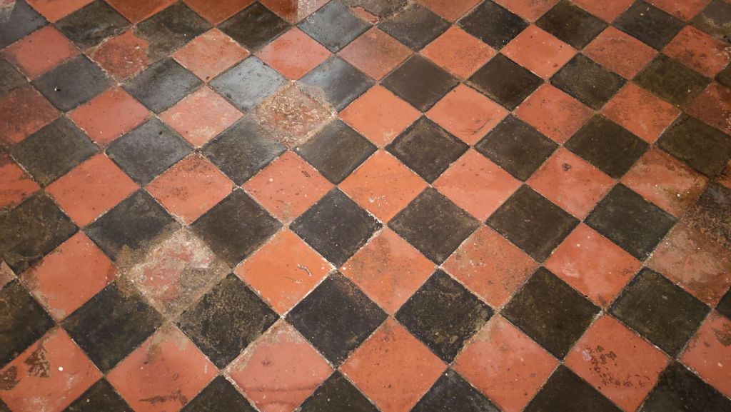 A checkerboard floor of red and black tiles, shown diagonally. The tiles are mostly intact but some are dirty or broken 