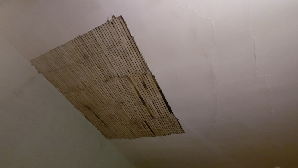 View looking up at a white ceiling a rectangle of wooden laths is exposed unplastered